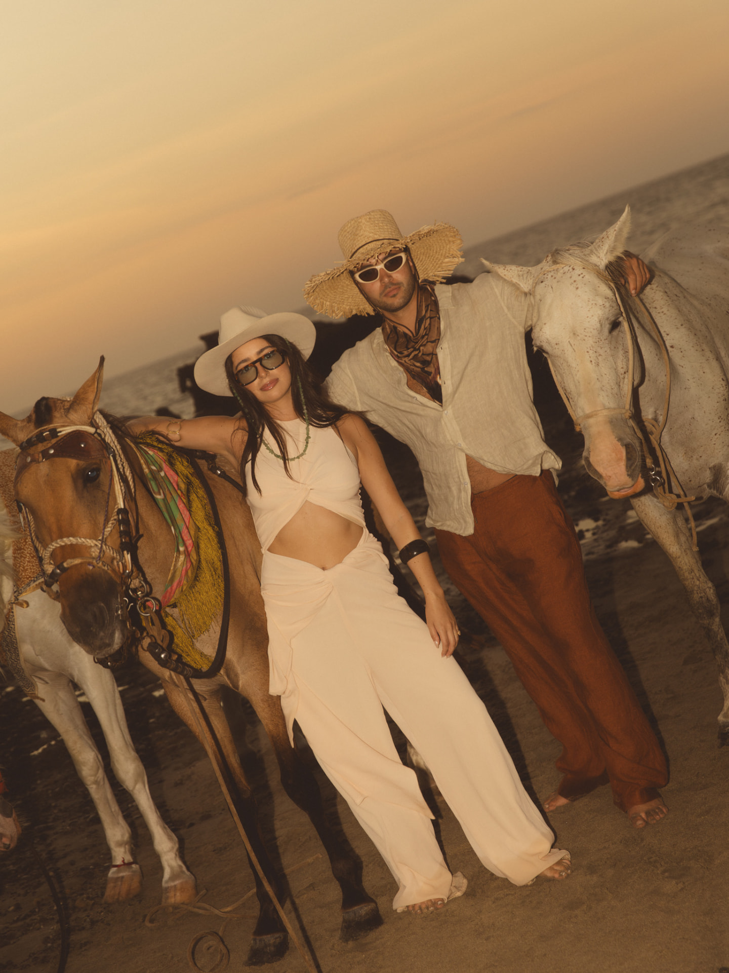 The couple posing with two horses on the beach at sunset